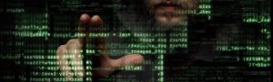 overlay of shadowy hacker reaching out to touch green code on screen