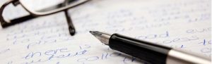 glasses and a pen atop a handwriting sample